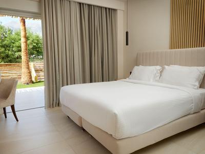 Camera d'hotel moderna con letto grande, scrivania e vista sul giardino attraverso una porta scorrevole in vetro.