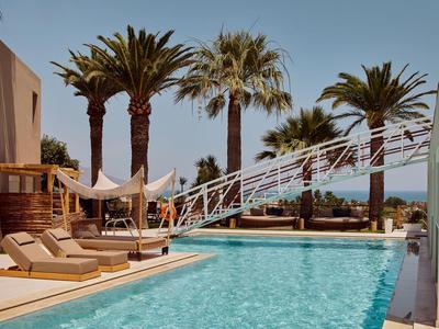 Area piscina moderna con lettini, palme e vista mare in una giornata di sole.