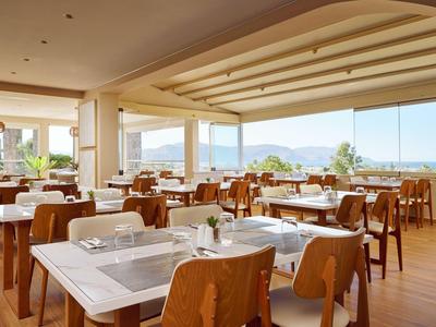 Ristorante luminoso con grandi finestre e vista sulle montagne, mobili in legno e tavoli apparecchiati.