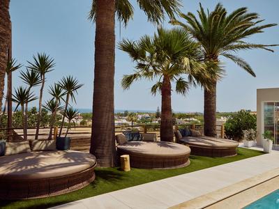 Area esterna con piscina, posti a sedere sotto palme e vista sulla costa