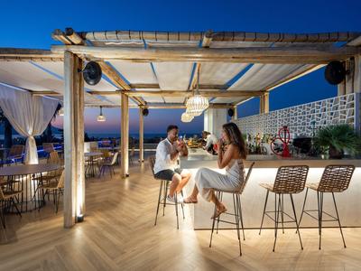 Area bar con posti a sedere al bancone, due persone che gustano bevande al tramonto.