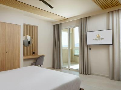 Modern hotel room with double bed, desk, TV, and balcony with curtains.