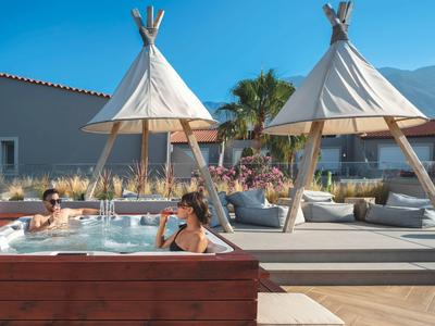 Outdoor-Whirlpool mit zwei Personen, Sonnendeck mit Kissen, weißen Tipis und Bergen im Hintergrund.