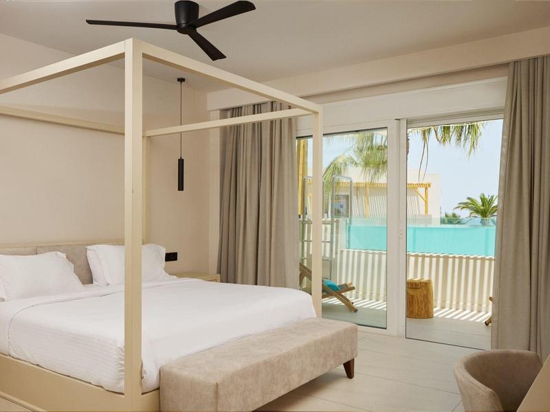 Bright hotel room with four-poster bed and terrace overlooking the sea.