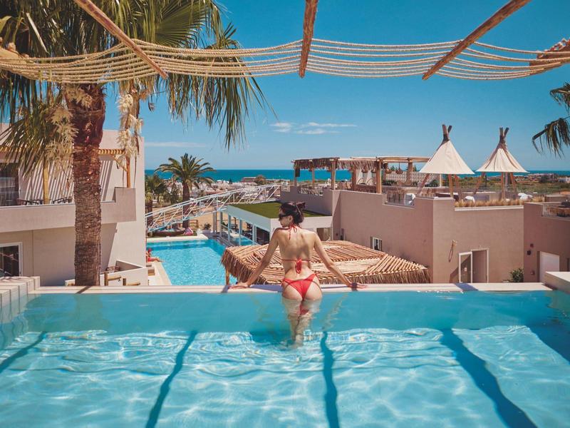 Woman sitting on the pool edge overlooking palm trees, lounge chairs, and the sea.