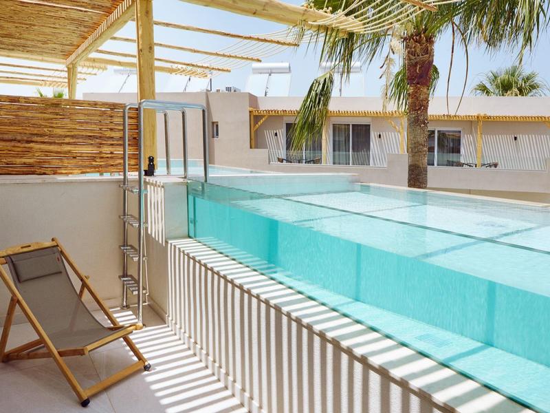 Modern pool area with glass swimming pool, wooden chairs, and palm trees on the terrace.