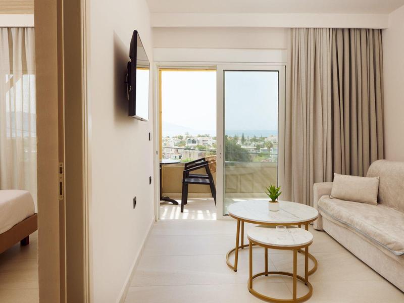 Bright hotel room with sofa, coffee table, and balcony with a view.