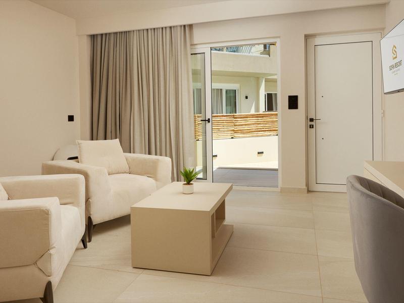 Bright hotel room with comfortable armchairs, low table, and access to a terrace.