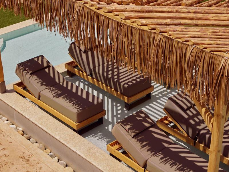 Cozy sun loungers with cushions under a thatched roof by the poolside.