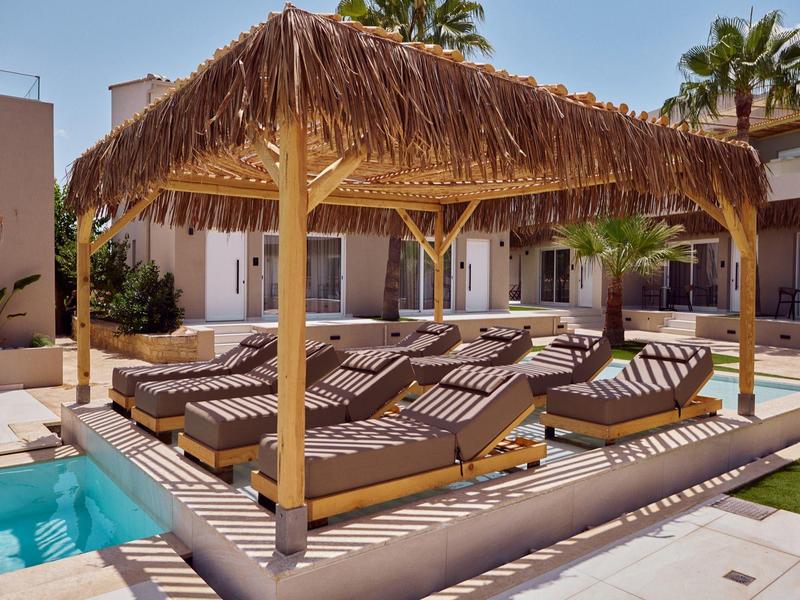 Pool area with loungers and thatched roof outdoors, surrounded by buildings