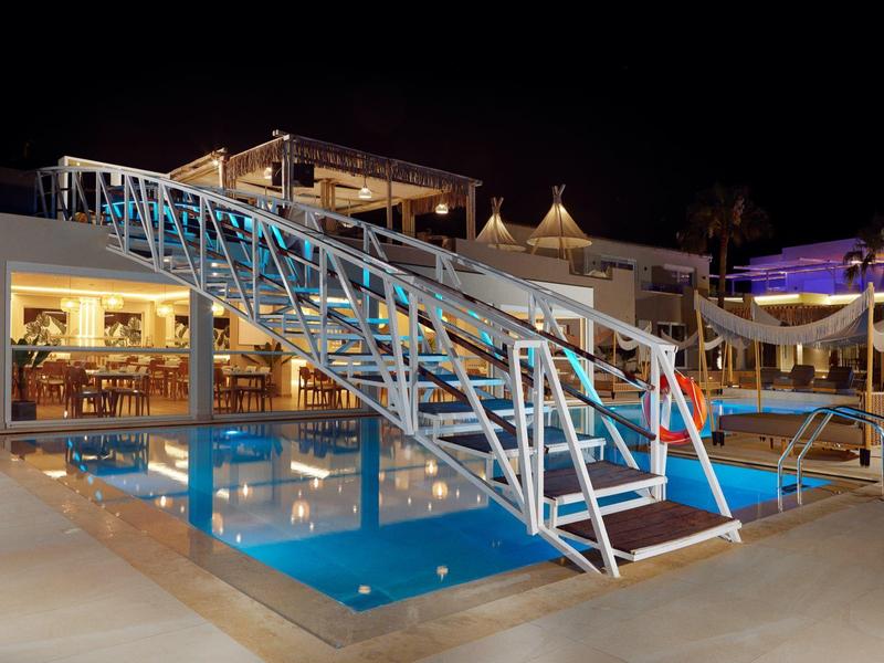 An illuminated pool with a metal bridge surrounded by a modern hotel at night.