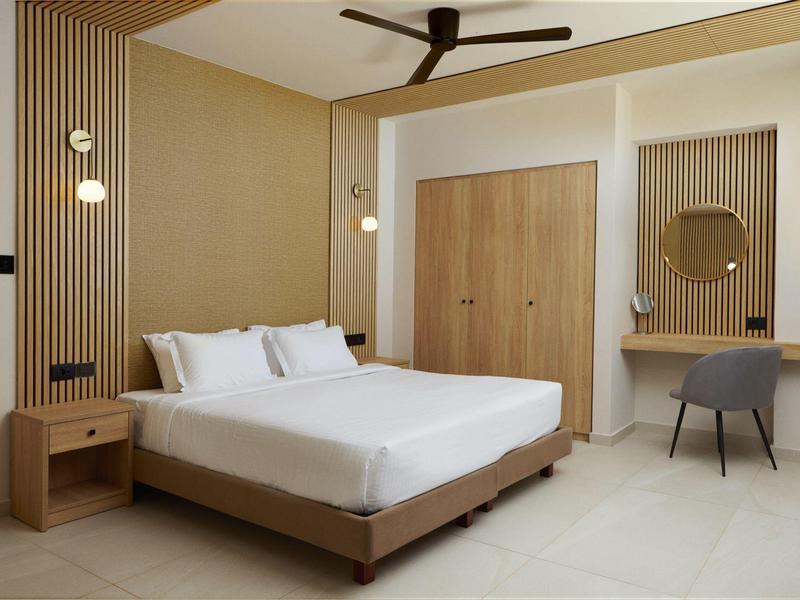 Modern hotel room with large bed, wooden panels, and a seating area.