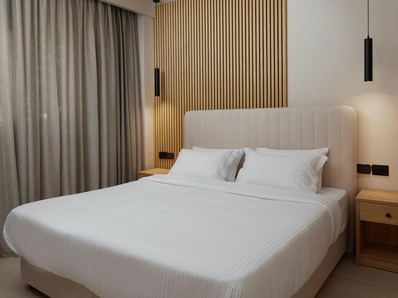 Modern hotel room with large bed, wooden accent wall, and simple nightstands.