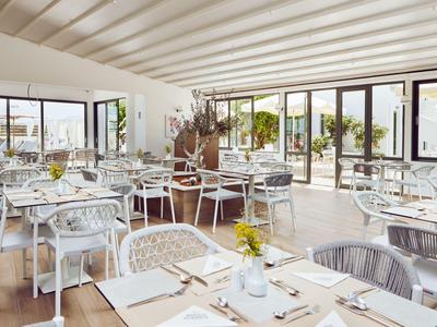 Hell eingerichteter Speisesaal mit vielen Tischen, Stühlen und großen Fenstern mit Blick ins Freie.