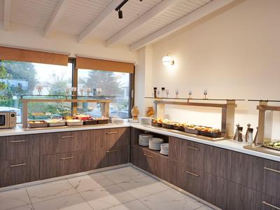 Moderne Küche mit Holzschränken, großen Fenstern, Mikrowelle und Speisebuffet auf Theke.
