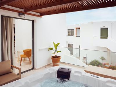 Balcón moderno con jacuzzi, plantas y vista a edificios blancos bajo cielo azul.