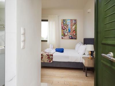 Blick in ein helles Schlafzimmer mit Doppelbett, buntem Bild und Nebenraum mit Waschbecken.