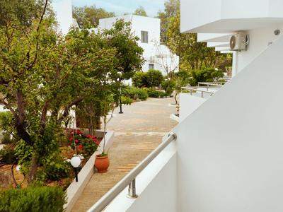 Vista desde un balcón blanco hacia un camino pavimentado y árboles verdes en un área de hotel.