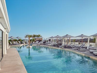 Moderne Hotelpoollandschaft mit Liegestühlen und Sonnenschirmen an einem sonnigen Tag.