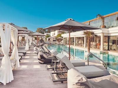 Moderner Hotelpoolbereich mit Liegestühlen, Sonnenschirmen und klar blauem Wasser bei klarem Himmel.