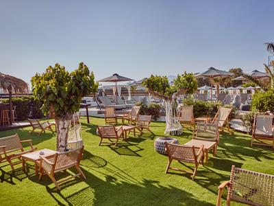 Garten mit Holztischen und Stühlen auf grünem Rasen unter klarem Himmel in Hotelanlage.