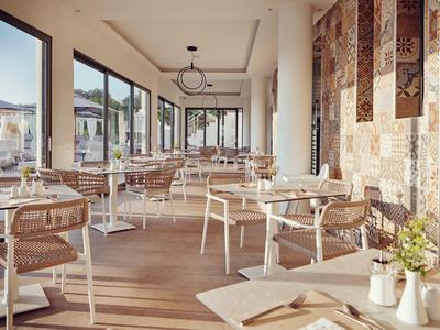 Helle Restaurant mit modernen Stühlen, großen Fenstern und dekorativen Wandbehängen.