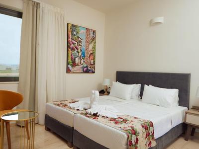 Helles Schlafzimmer mit zwei Einzelbetten, grauem Kopfteil, buntem Bild und gelbem Sessel.