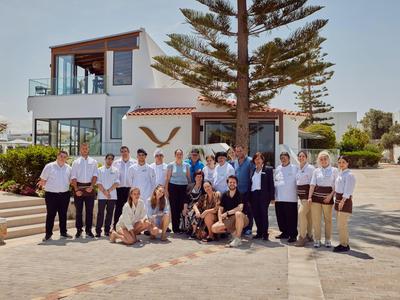 Un gruppo di persone posa davanti a un moderno edificio bianco di un hotel con alberi e cielo sereno.