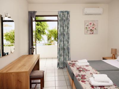 Helles Schlafzimmer mit Holzmöbeln, Doppelbett, buntem Vorhang und offener Tür zum Balkon.