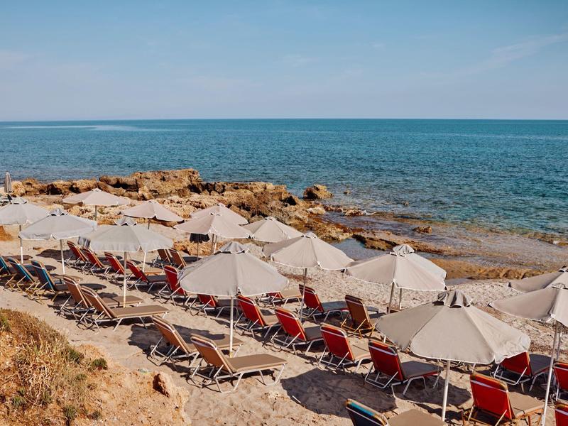 Playa con tumbonas rojas y sombrillas blancas junto al mar tranquilo bajo un cielo azul.