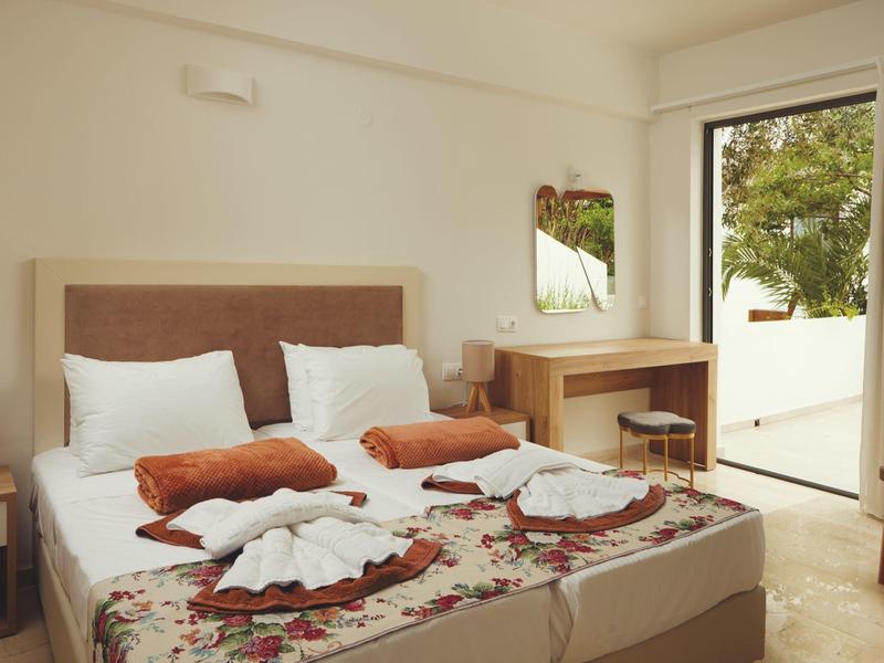 Habitación de hotel luminosa con cama doble, tres toallas y acceso a un balcón con plantas verdes.