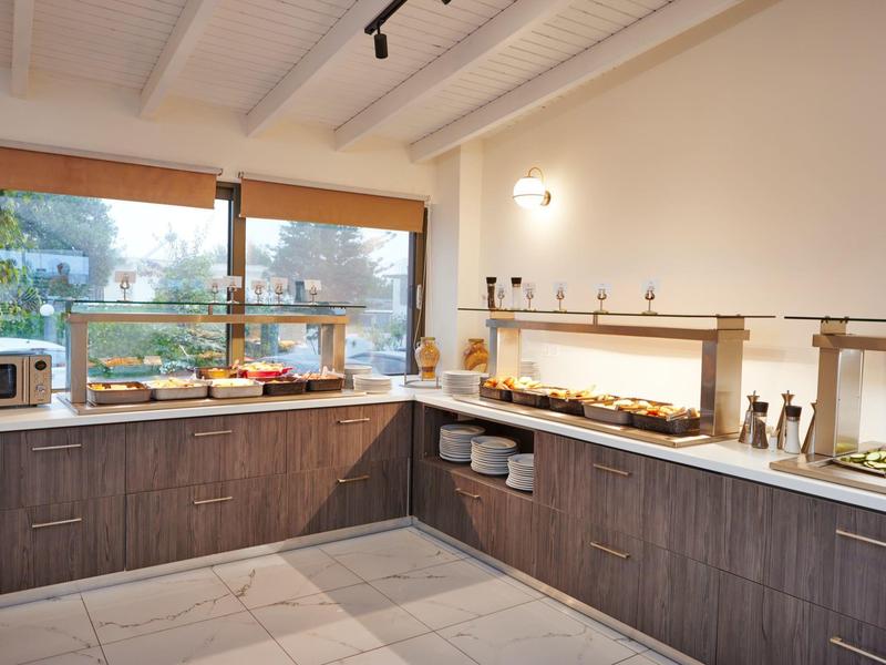 Área de buffet con mostradores, varios alimentos, microondas y grandes ventanas hacia el exterior.