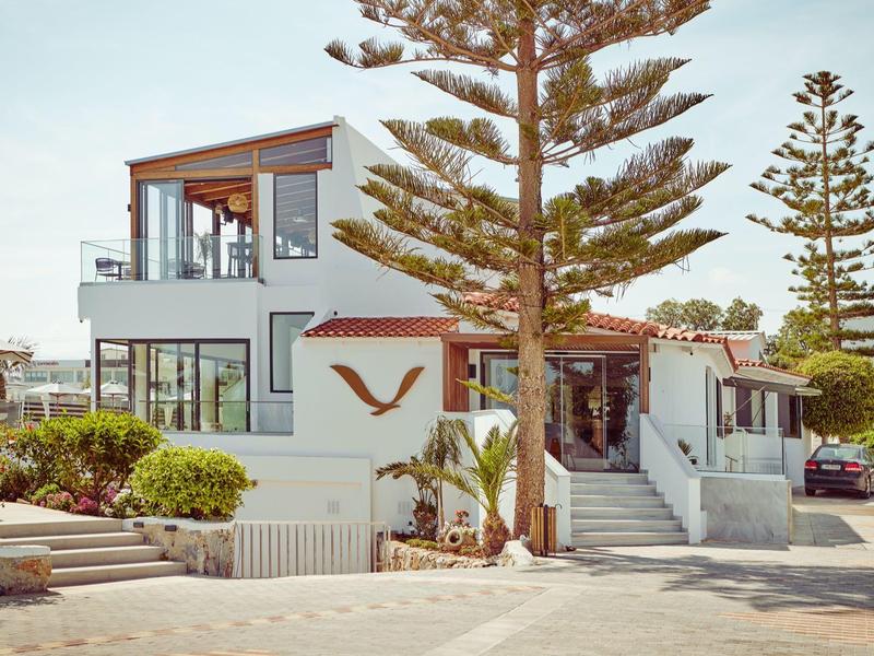 Casa de vacaciones moderna con grandes ventanas, rodeada de árboles y estacionamientos.