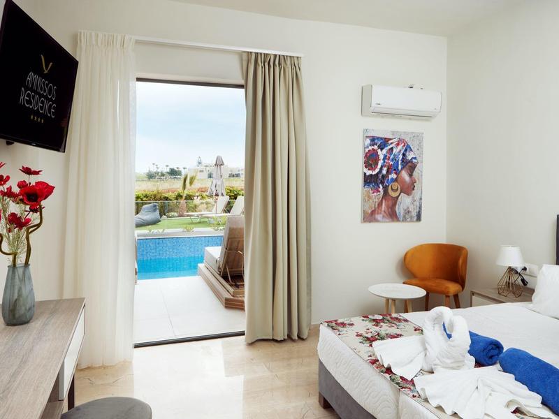 Habitación de hotel luminosa con cortina abierta, vista a la piscina y terraza, cama blanca y decoraciones.