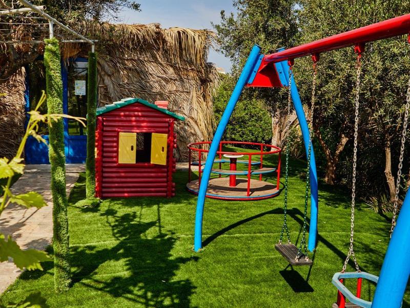 Parque infantil colorido con columpios, tobogán y casa de juego sobre césped verde bajo cielo azul.