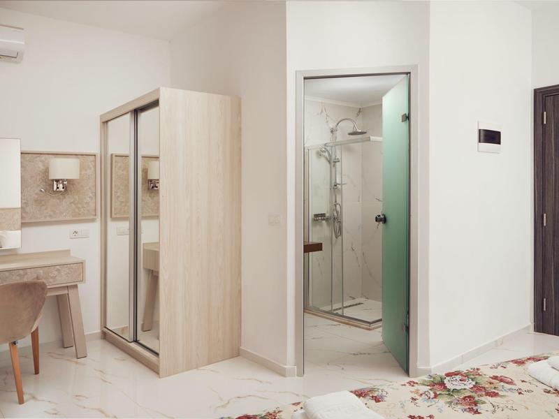 Habitación de hotel luminosa con tocador, armario y baño con ducha de vidrio.