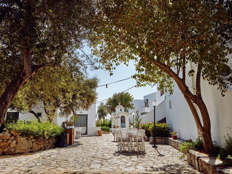 Patio con suelo empedrado, paredes blancas, árboles y mesas en una tranquila zona del hotel.