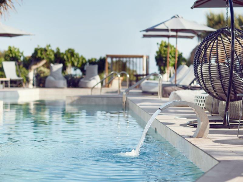 Piscina exterior moderna con tumbonas, sombrillas y decoración en el jardín del hotel bajo el sol.