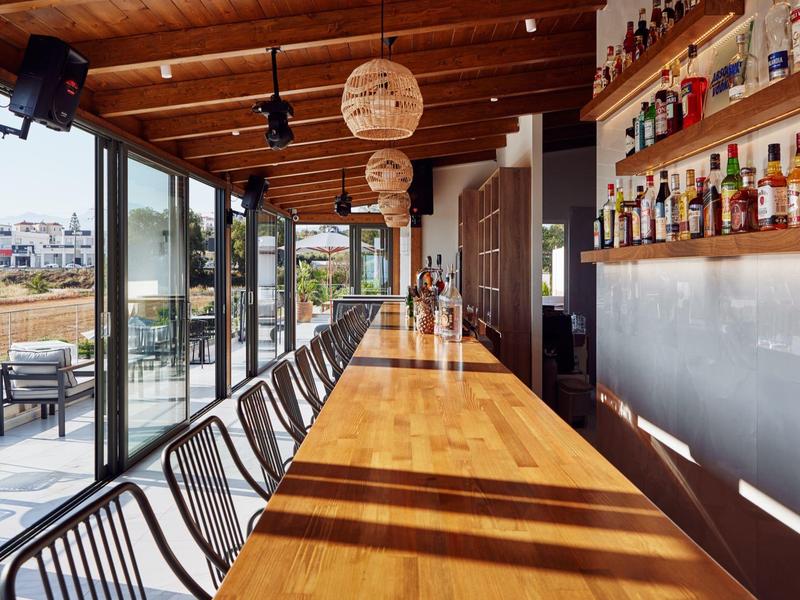 Área de bar moderna con barra de madera, taburetes y grandes ventanales con vista a la terraza.