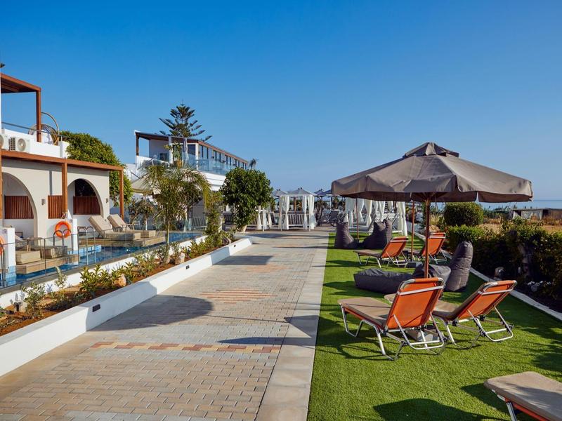 Terraza de hotel con tumbonas, sombrillas y vista a un jardín verde bajo cielo despejado.