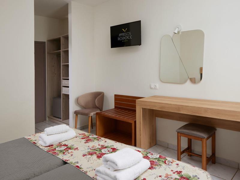 Habitación de hotel sencilla con dos camas, una silla, mesa y televisor en la pared.