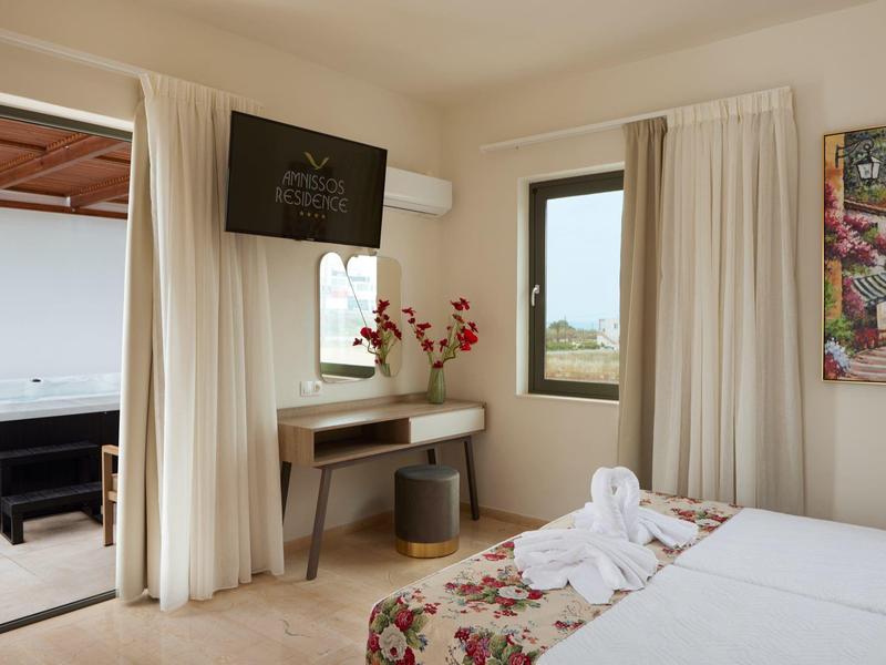 Habitación de hotel luminosa con cama, escritorio, decoración floral y acceso a una terraza con vista al mar.
