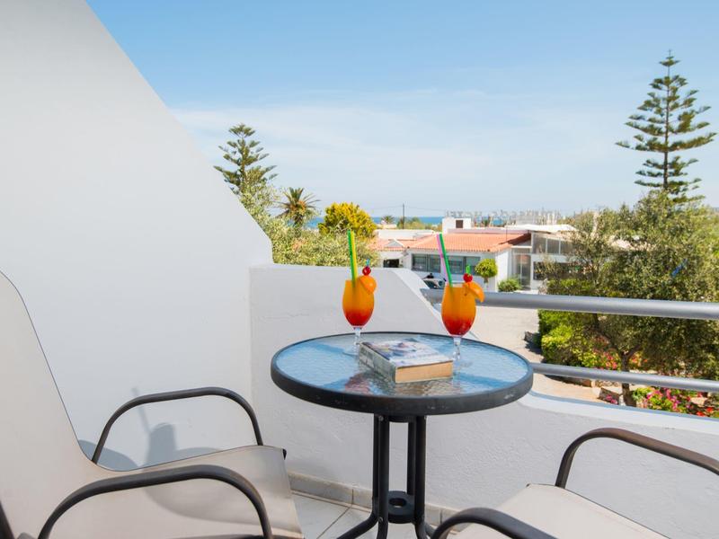 Balcón con mesa, dos cócteles y dos sillas con vista a árboles y casas.