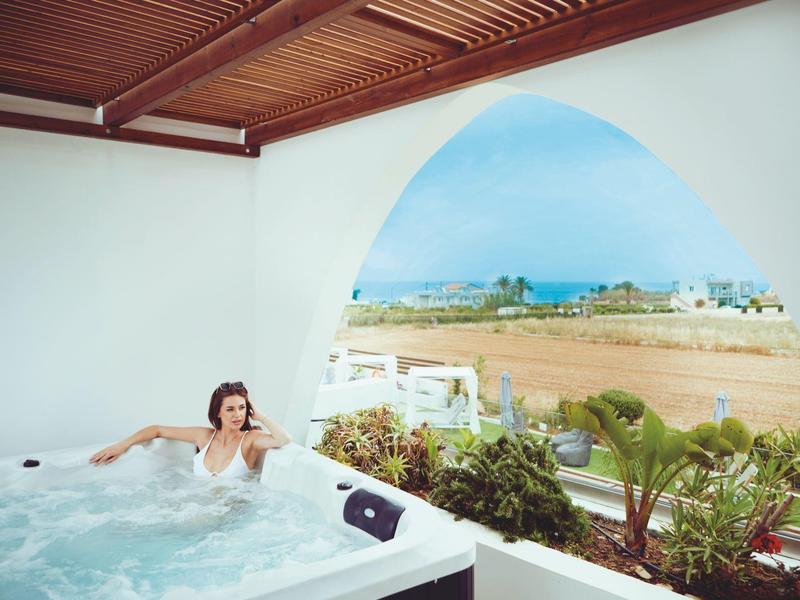Mujer relajándose en jacuzzi con vista a paisaje tropical y mar a través de ventana en arco.