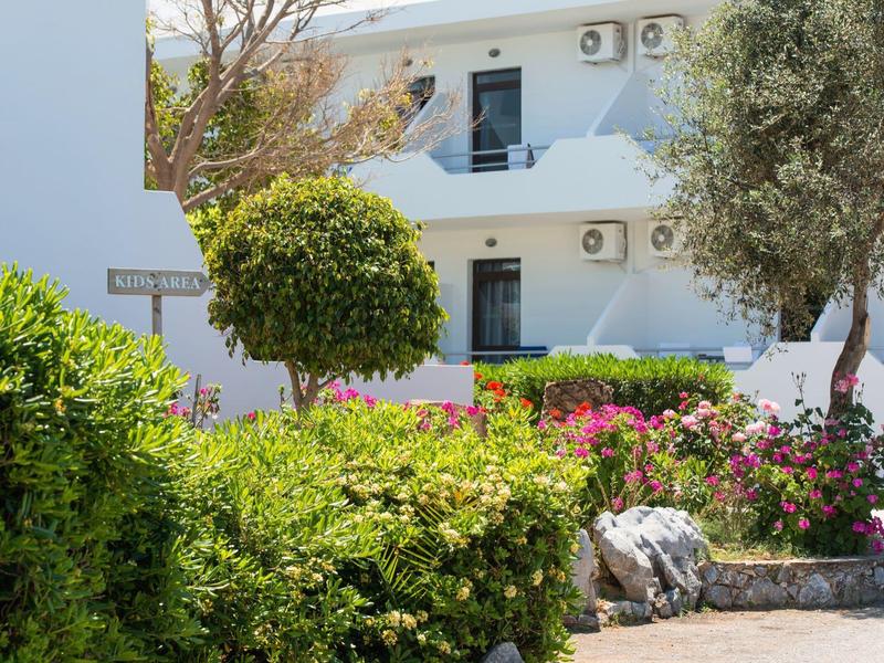 Edificio del hotel con paredes blancas, arbustos verdes y flores en el área del jardín.