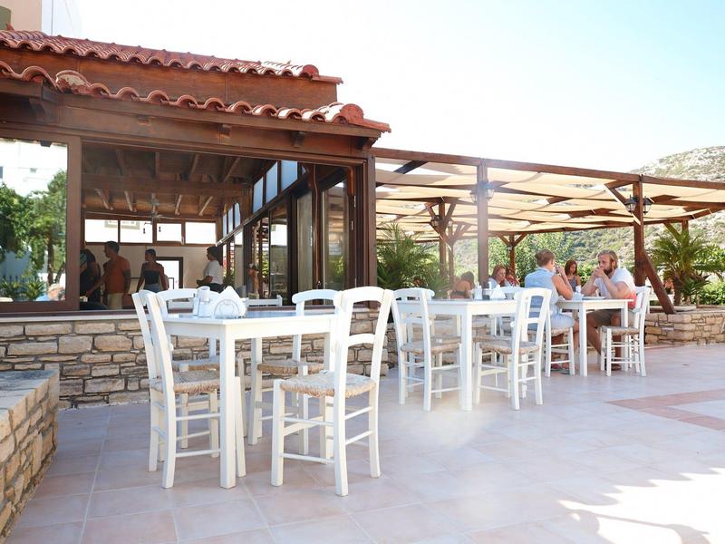 Buitenrestaurant met witte houten tafels en stoelen op een betegeld terras bij daglicht.