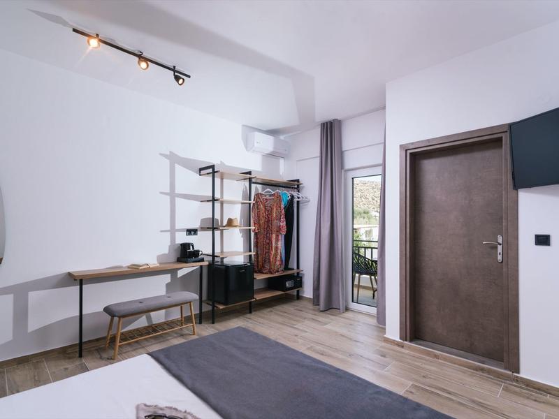 Lichte hotelkamer met kledingrek, bureau, stoel en balkon met uitzicht naar buiten.