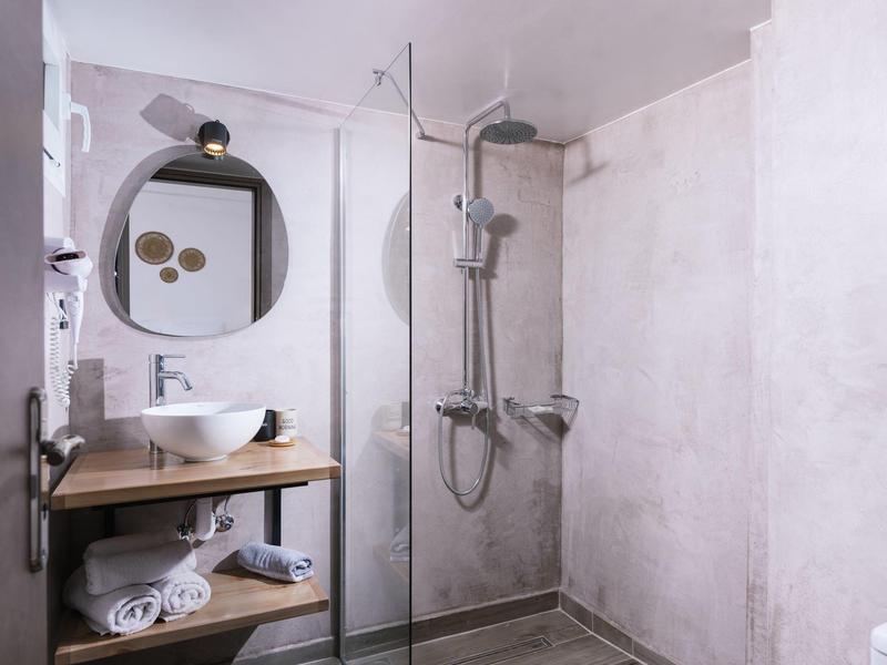 Moderne douche met glazen scheidingswand, ronde spiegel en open houten plank met handdoeken.