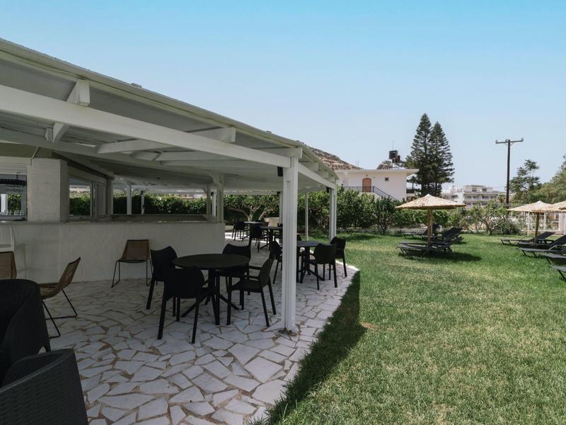 Buitengebied van hotel met tafels, stoelen en tuin onder heldere lucht.