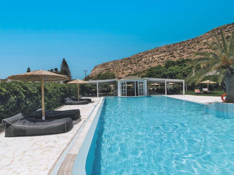 Een buitenzwembad met parasols tegen heuvels en een heldere blauwe lucht.